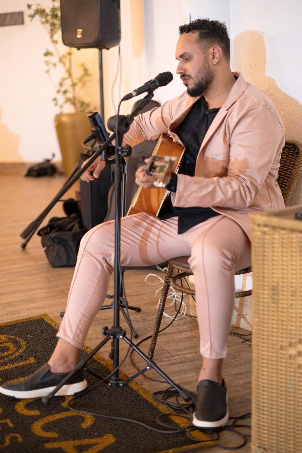 Lucca Borges tocando violão com terno rosa
